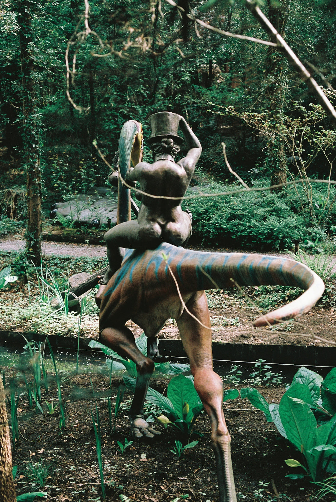 Bronze sculpture of person riding a dinosaur in a garden